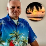 A man in a hawaiian shirt standing next to a wall.